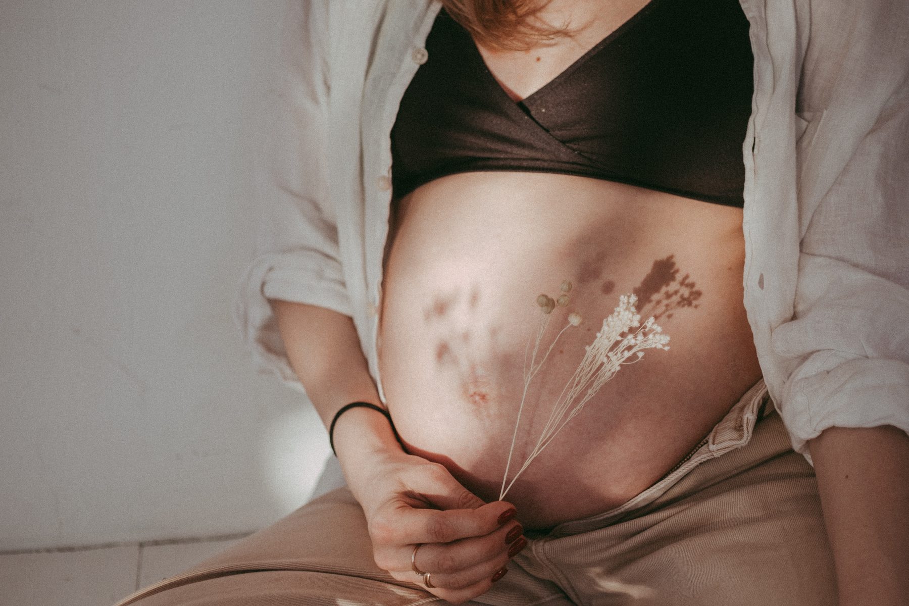Close-up of a pregnant belly in neutral tones, with dried flowers