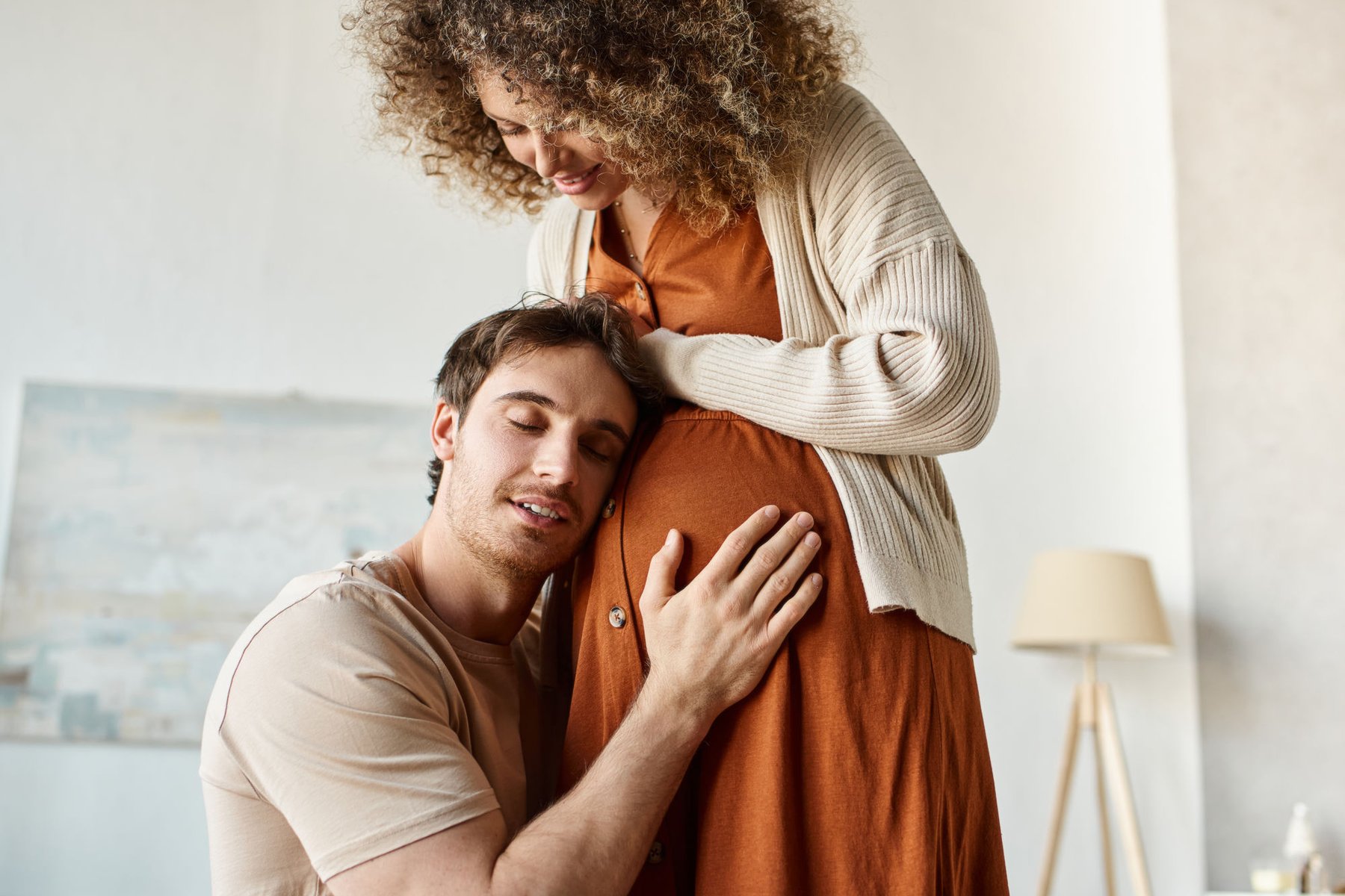 A partner resting their head against a pregnant belly in a loving embrace
