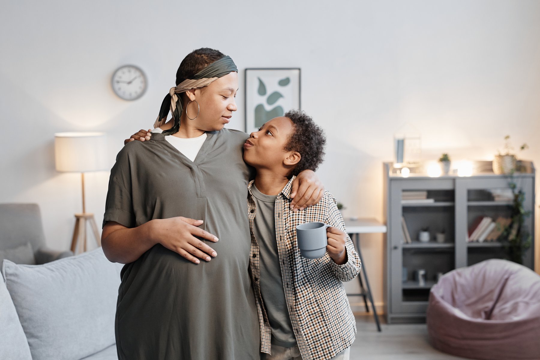 A pregnant parent embracing their child in a warm living room