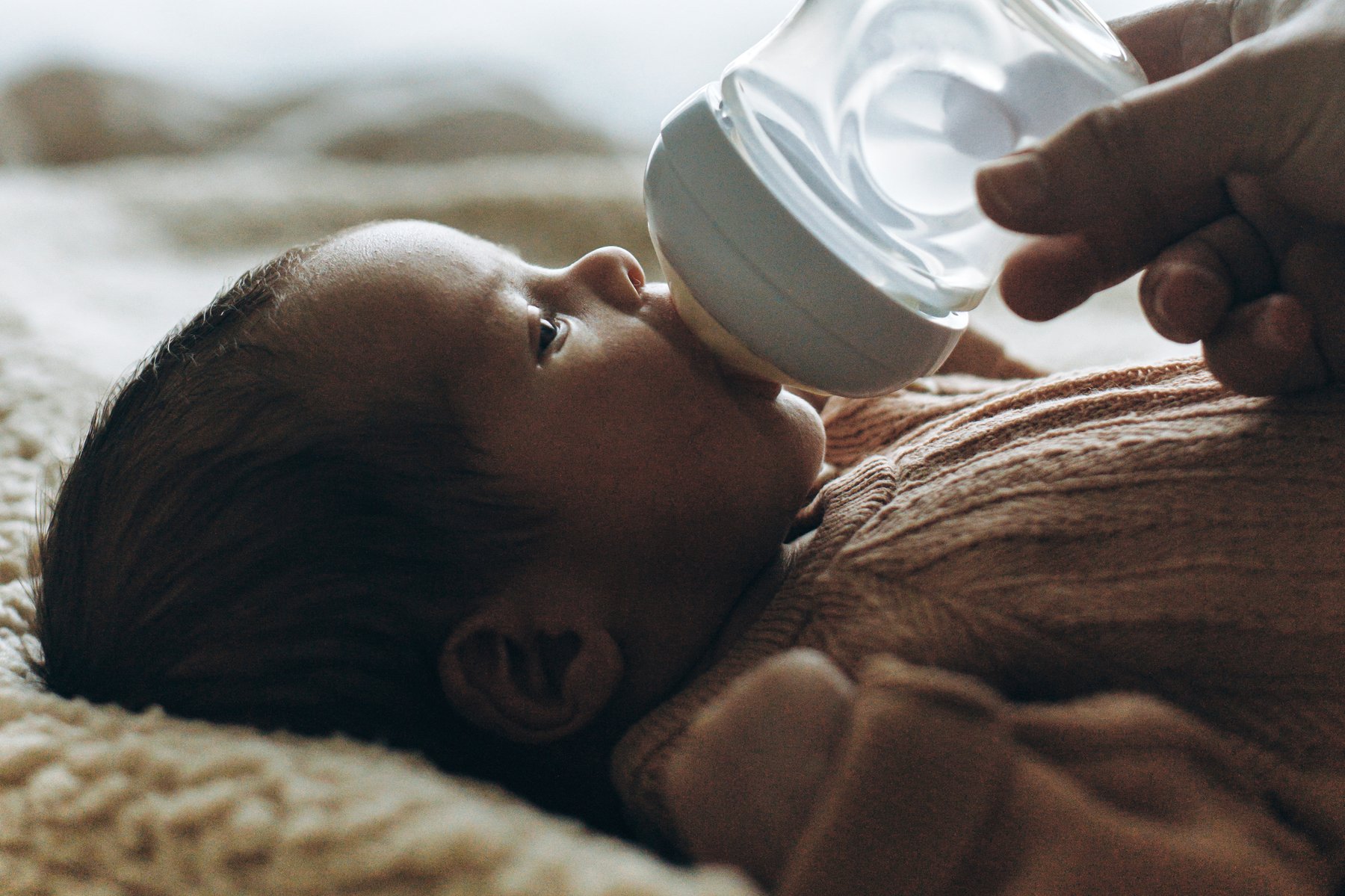 A parent bottle-feeding a newborn in soft window light