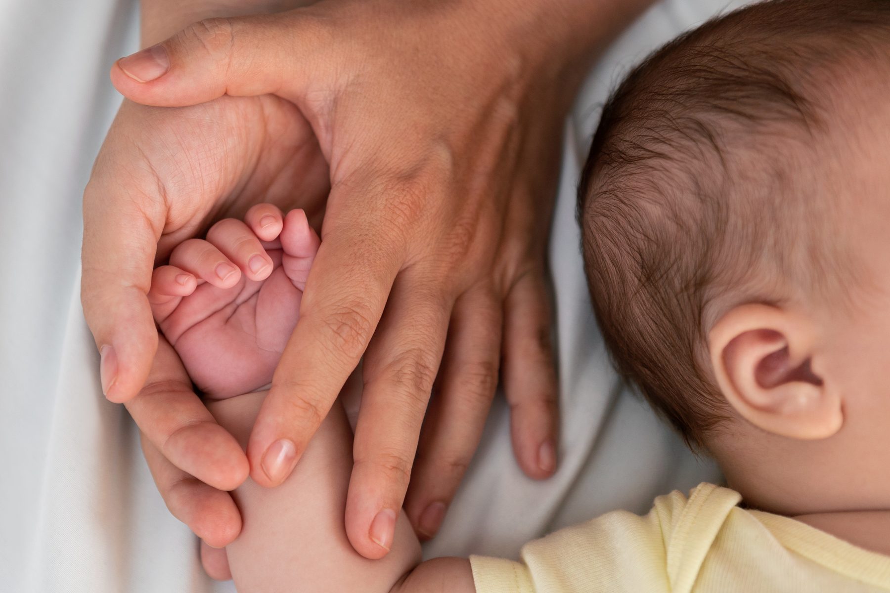 A parent's hands cupped gently around a newborn's hand as the baby rests