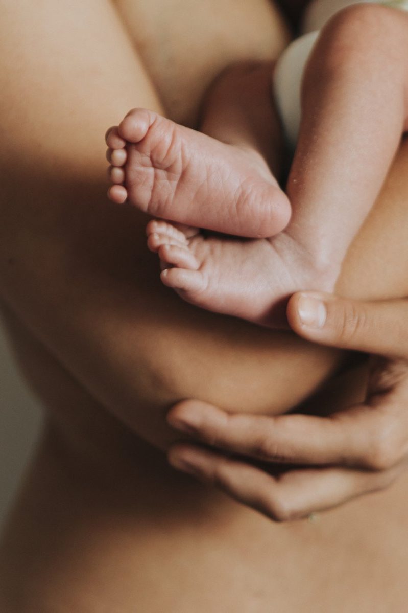A newborn's feet cradled gently within a parent's crossed arms