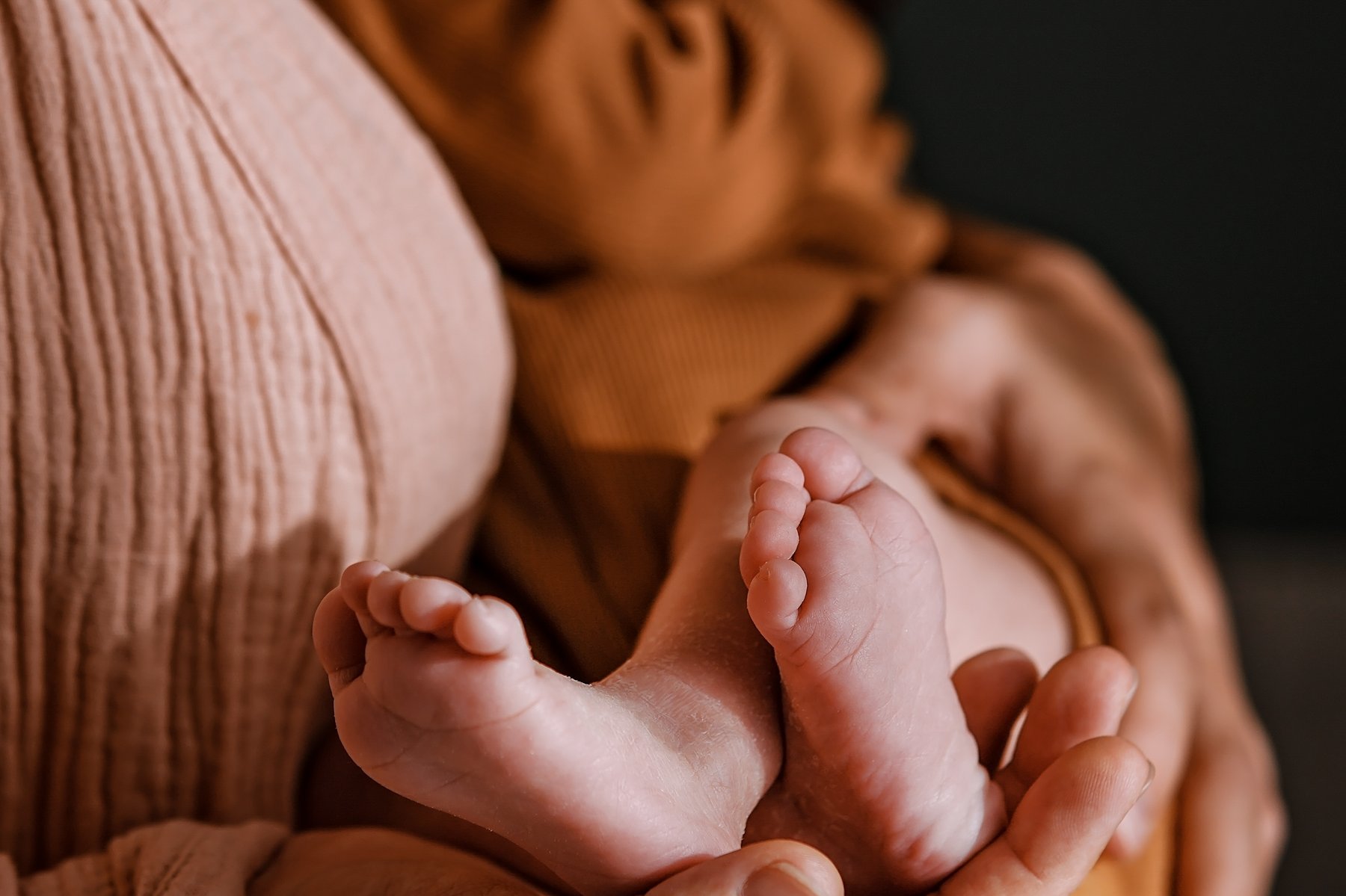 A newborn's feet held gently while swaddled against a parent's chest