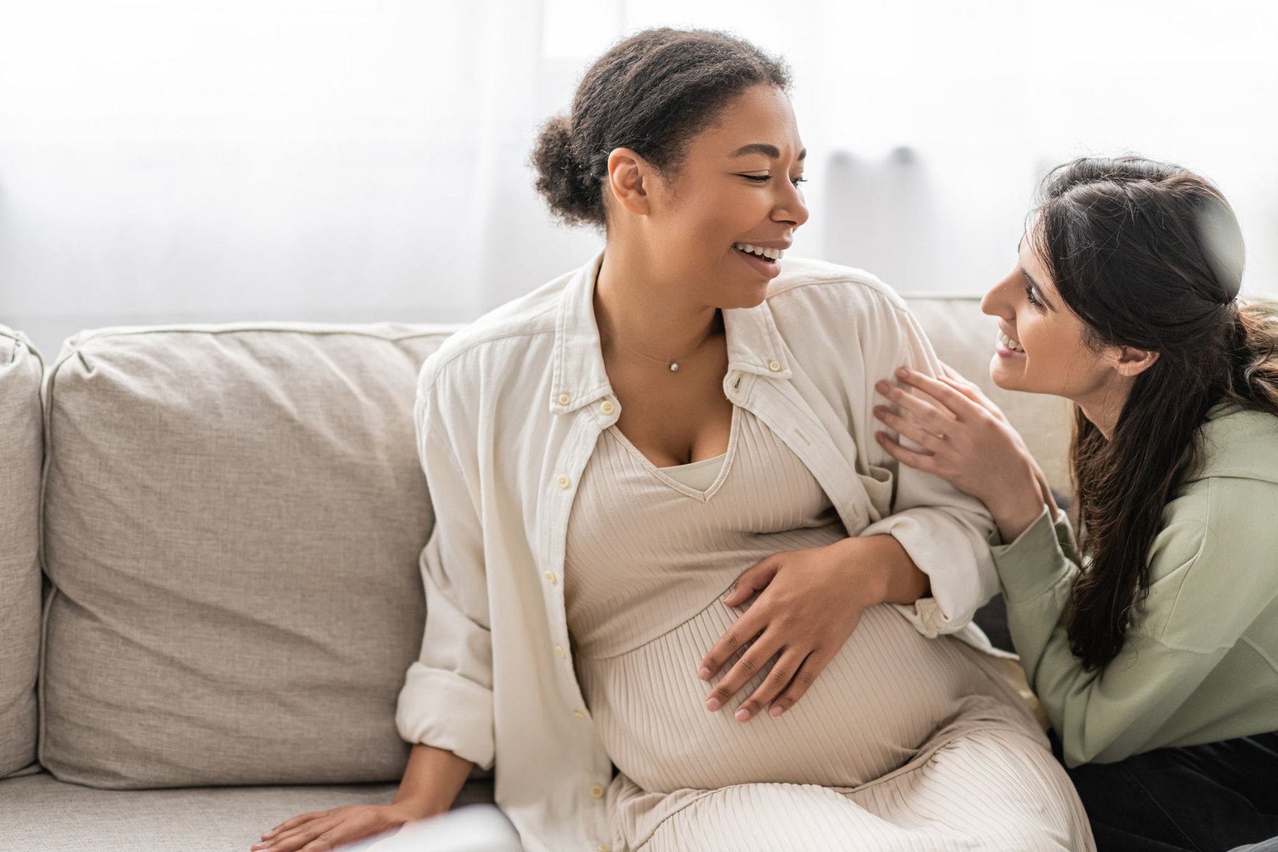 A pregnant woman laughing with her partner, hand resting supportively on her shoulder