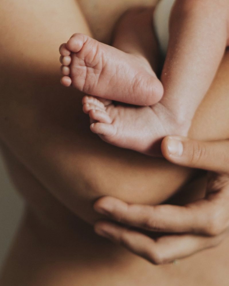 A newborn&rsquo;s feet cradled in a parent&rsquo;s crossed arms